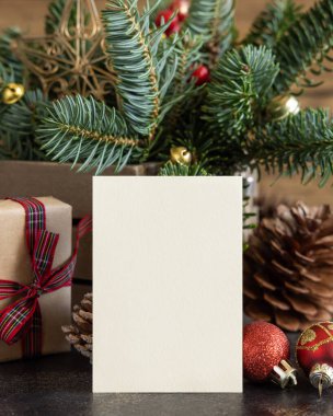 Vertical blank card between decorations, fir branches and pine cones close up, mockup. Christmas or New Year greeting card template, Holiday or wedding stationery