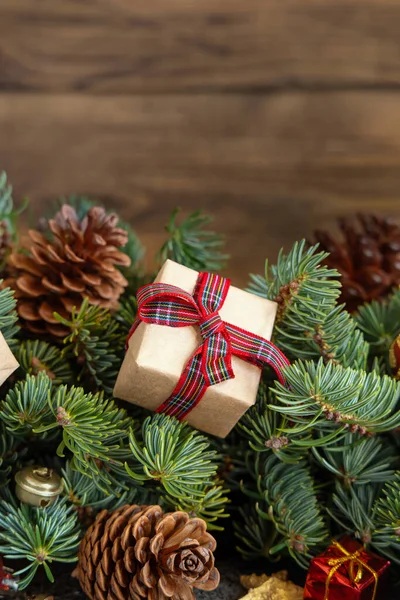 クリスマスの装飾の近くの赤いモミの枝にギフトボックスを包み 木製の背景に松のコーンを閉じ スペースをコピーします クリスマスや新年の休日の雰囲気 — ストック写真
