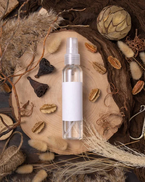 Transparent Refillable spray bottle on wood near natural boho decorations top view, label mockup. Skincare beauty product, lotion or essence. Bohemian eco friendly cosmetics flat lay with dried leave
