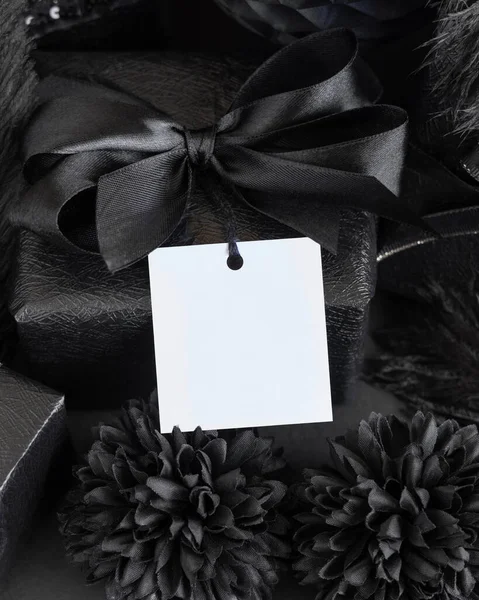 Wrapped Gift Boxes with black paper flowers and decorations and square gift tag, mockup, copy space. Dark composition with blank label card for Birthday, Anniversary or black party present