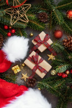 Noel süsleri, Noel Baba şapkası ve koyu siyah arka planda yeşil köknar dalları arasında paketlenmiş hediye kutuları. Noel ya da Yeni Yıl Tatil atmosferi düzdü