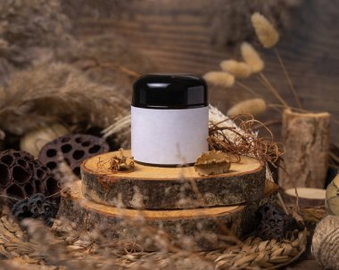 Doğal dekorasyonların yanında boş etiketli krema kavanozu kapanıyor, paket maketi. Çevre dostu cilt bakım ürünü, losyon ya da krem. Kurumuş yapraklar ve çiçeklerle bohem kompozisyonu