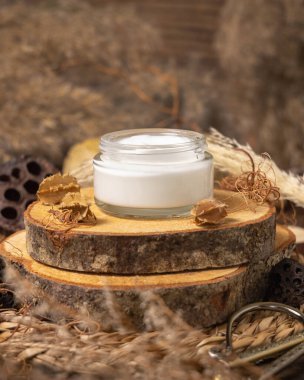 Opened glass cream jar on wood near natural decorations close up, package mockup. Eco friendly skincare product, lotion or cream. Bohemian composition with dried leaves and flower