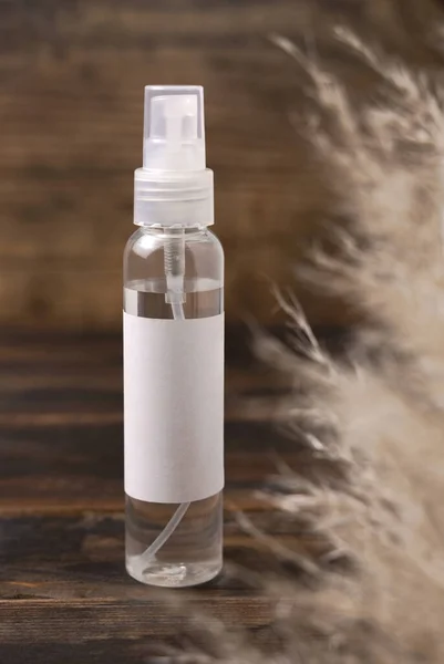 Transparent spray bottle on wood near pampas grass close up, label mockup. Skincare beauty product, cleanser or water. Bohemian eco friendly cosmetics with dried leave