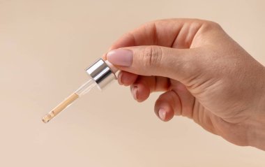 Dişi El pipeti tutuyor ve açık bej üzerine düşüyor. Doğal cilt bakımı ürünü, serum ya da temel yağ. Kozmetik rutini. Tıbbi araştırma 