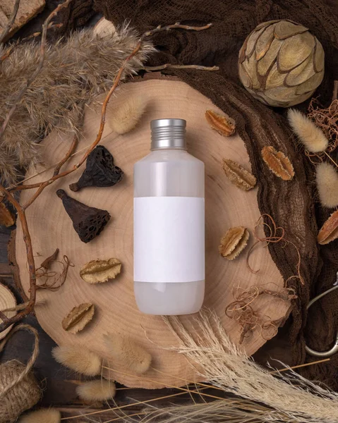 Bottle blank label on wood near natural boho decorations top view, cosmetic package mockup. Eco friendly skincare product, lotion or cream. Bohemian flat lay with dried leaves and flower