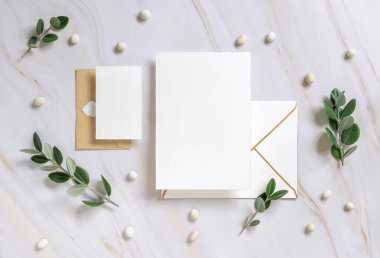 Kartlar ve zarf okaliptüs dalları ve çakıl taşlarının yakınındaki mermer bir masada Mockup. Düğün kırtasiyesi setiyle romantik bir daire. Minimum bileşim. Doğaya yakın. 