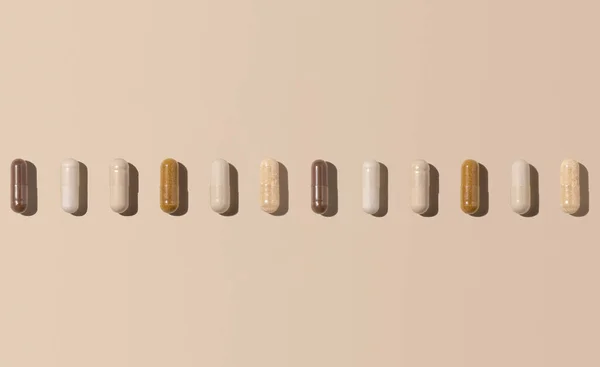 Mix of medical capsules in a line on light beige top view, hard shadows. Preventive medicine and healthcare, dietary supplements and vitamins.  Assorted pharmaceutical medicine capsules