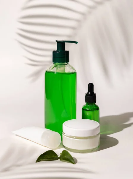 Refillable Cosmetic bottles, jar and tube with green liquid on white, Palm leaf hard shadows, close up, mockup. Skincare beauty products. Natural cosmetics with aloe ver