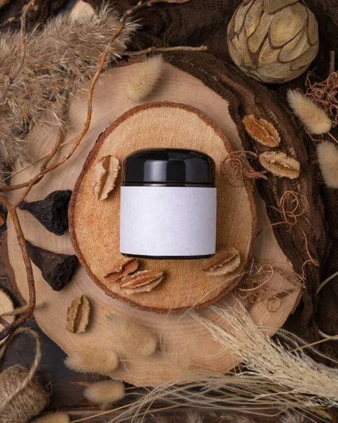 Cream jar with blank label on wood near natural boho decorations top view, cosmetic packaging mockup. Skincare product for everyday beauty routine. Bohemian eco friendly flat lay with dried leave