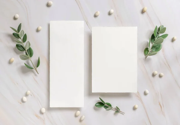 Vertical cards on a marble table decorated with eucalyptus branches and white stones top view, Wedding Mockup. Romantic flat lay with blank menu card. Minimal composition. Close to nature
