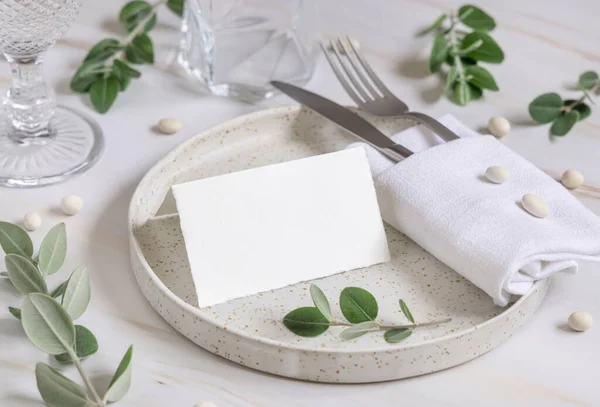Elegant Table setting with a folded card decorated with eucalyptus branches close up, Wedding Mockup. Romantic table with horizontal blank card. Close to nature and simplicity concepts