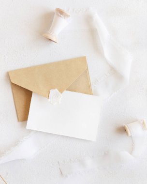 İpek kurdelelerin yanındaki boş kart ve zarf beyazın üstünde, maket. Yatay kartlı romantik bir sahne. Bohem selamlaması ya da düğün davetiyesi