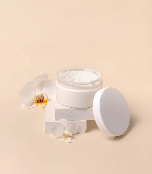 Opened Cream jar with a blank white lid near white orchid flowers on light yellow close up. Cosmetic packaging Mockup. Exotic natural cosmetics, romantic composition, everyday skincare routin