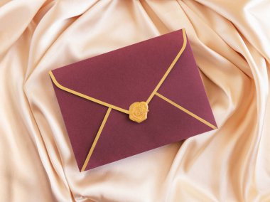 Bej renkli ipek kumaş üst görünümde kırmızı mühürlü zarf kartı, maket. Zarflı romantik sahne, selamlama veya düğün davetiyesi.