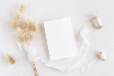 İpek kurdelelerin yanındaki boş kart ve kurutulmuş tavşanın kuyruğundaki çim beyaz, maket. Boho romantik sahnesi ve dikey kart. Bohem ya da doğaya yakın selamlama ya da düğün davetiyesi