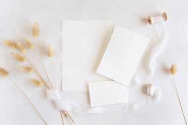 İpek kurdelelerin yanındaki boş kartlar ve kurutulmuş tavşanın kuyruğundaki çim beyaz, maket. Kartlarla boho romantik sahnesi. Bohem ya da doğaya yakın selamlama ya da düğün davetiyesi