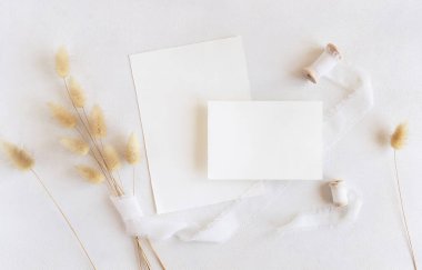 İpek kurdelelerin yanındaki boş kartlar ve kurutulmuş tavşanın kuyruğundaki çim beyaz, maket. Dikey kartlarla boho romantik sahnesi. Bohem ya da doğaya yakın selamlama ya da düğün davetiyesi