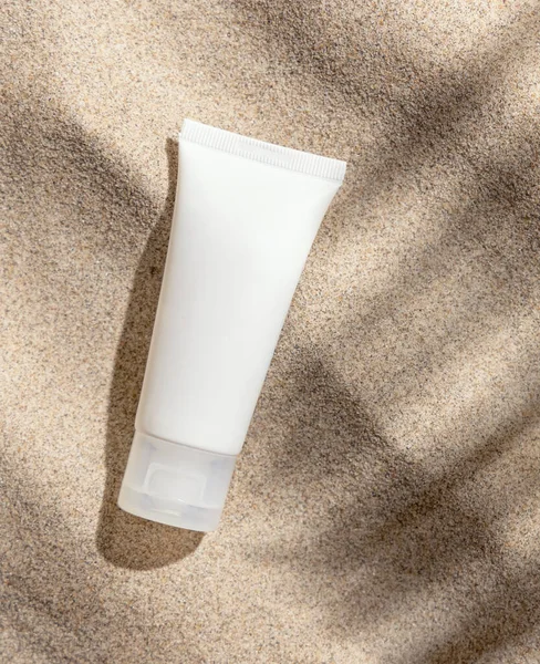 White ceam tube on beige sand top view. Packaging mockup. Natural skincare product for beauty routine. Summer sunny day with palm leaf hard shadow, tropical vacation mood