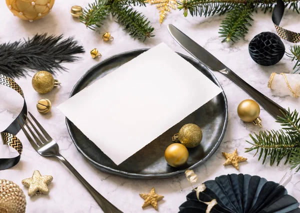 Black and golden Table setting with ornaments and fir tree branches close up, invitation card mockup. Christmas or New Year atmospheric composition on marble table, copy space.