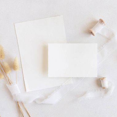 İpek kurdelelerin yanındaki boş kartlar ve kurutulmuş tavşanın kuyruğundaki çim beyaz, maket. Dikey kartlarla boho romantik sahnesi. Bohem ya da doğaya yakın selamlama ya da düğün davetiyesi