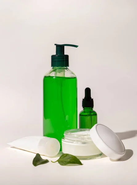 Refillable Cosmetic bottles, jar and tube near green leaves on white, bottles filled with green liquid, close up, mockup. Skincare beauty products. Natural cosmetics with aloe ver
