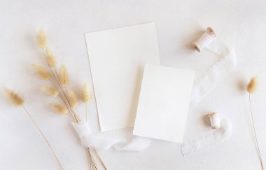 İpek kurdelelerin yanındaki boş kartlar ve kurutulmuş tavşanın kuyruğundaki çim beyaz, maket. Dikey kartlarla boho romantik sahnesi. Bohem ya da doğaya yakın selamlama ya da düğün davetiyesi