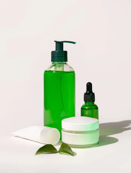 Refillable Cosmetic bottles, jar and tube near green leaves on white, bottles filled with green liquid, close up, mockup. Skincare beauty products. Natural cosmetics with aloe ver