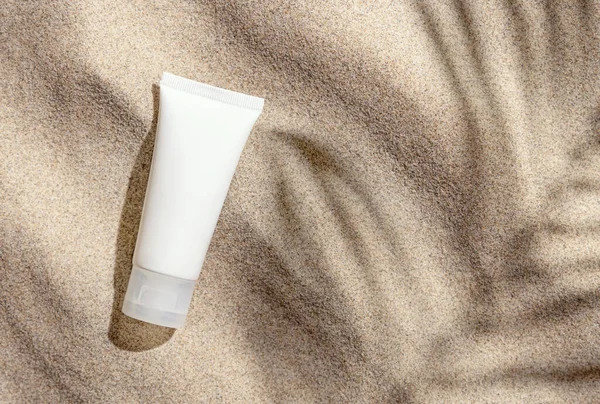 White ceam tube on beige sand top view. Packaging mockup. Natural skincare product for beauty routine. Summer sunny day with palm leaf hard shadow, tropical vacation mood