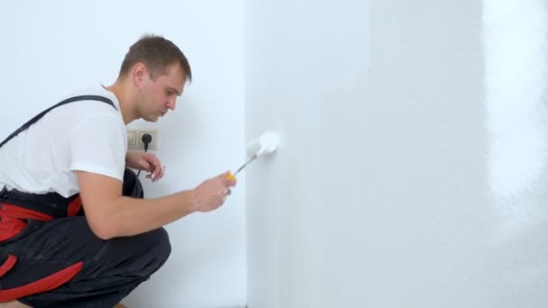 Joven pinta la pared en la habitación con un rodillo de pintura blanca — Vídeos de Stock