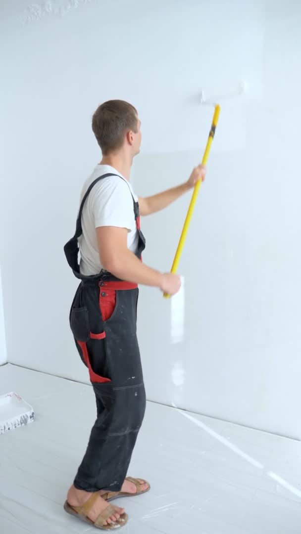 Jongeman schildert de muur in de kamer met een roller witte verf, verticaal — Stockvideo