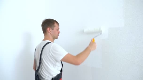 Genç adam odanın duvarını beyaz bir boyayla boyuyor. — Stok video