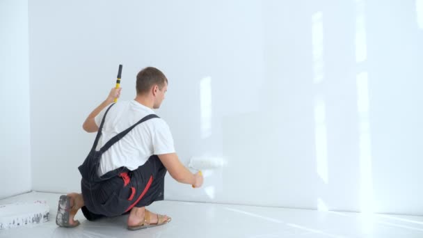 Jongeman schildert de muur in de kamer met een roller witte verf — Stockvideo