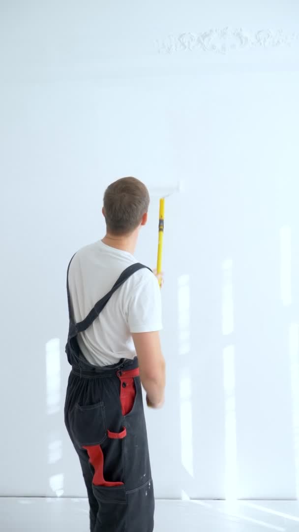 Jongeman schildert de muur in de kamer met een roller witte verf, verticaal — Stockvideo