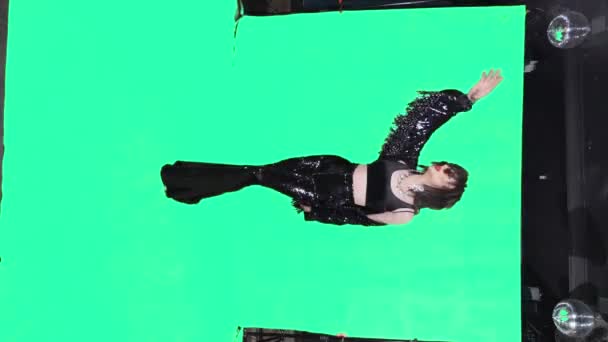 Vertically. travesty actor in black flared trousers and a black leather jacket, dances and sings in full growth on a green background — Stok video