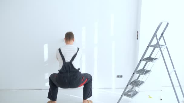 Back view of a man in overalls painting a wall with white paint — Stock video