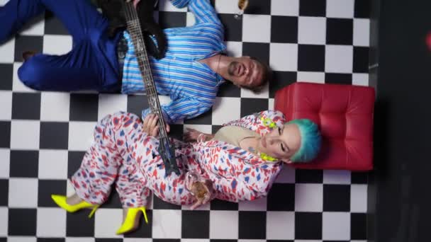 A couple, a man playing the electric guitar and a travesty actor lie on the floor with a checkerboard pattern. rotating image — Video Stock
