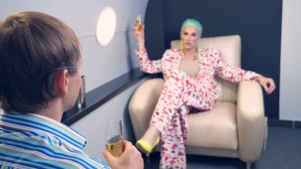 A respectable man and a guy in womens clothes, with makeup and a blue wig, drink champagne in a VIP plane — Stock Video