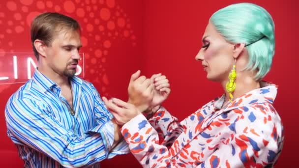 Travesty actor in a blue wig handcuffs a handsome guy in a red room — Video