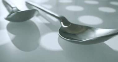 extreme close-up, detailed. large and small stainless steel spoons on a white glossy surface