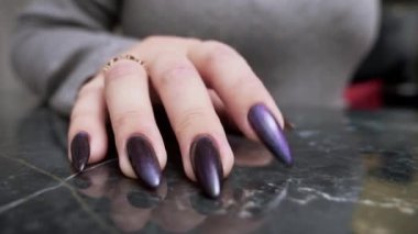 close-up of a female hand with long black nails impatiently tapping her fingers on a reflective black surface