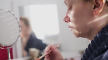 close-up of a womans face. woman doing makeup while sitting in front of a mirror at home