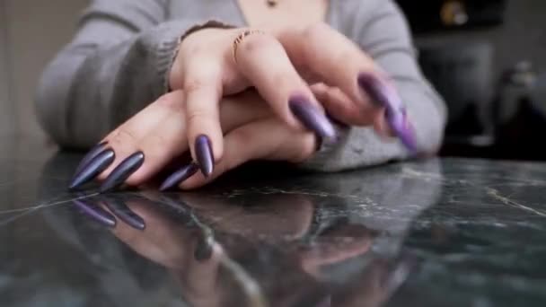 Close-up of a female hand with long black nails impatiently tapping her fingers on a reflective black surface — Wideo stockowe