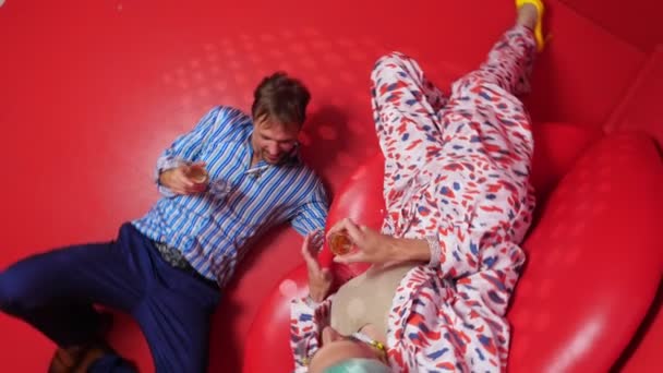 Top view, rotating image. in the red room, a transvestite sits on a couch, next to her a man lies on the floor — Stockvideo