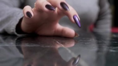 close-up of a female hand with long black nails impatiently tapping her fingers on a reflective black surface