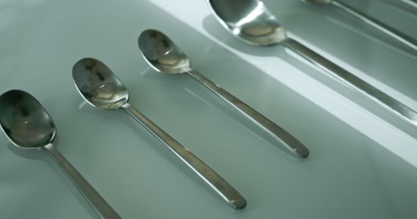 Extreme close-up, detailed. large and small stainless steel spoons on a white glossy surface — Video