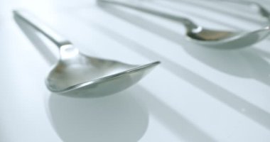 extreme close-up, detailed. large and small stainless steel spoons on a white glossy surface