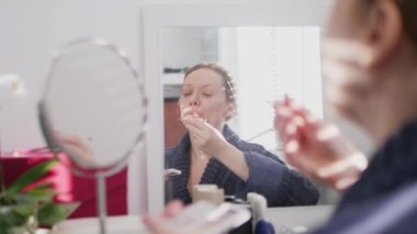 close-up of a womans face. woman doing makeup while sitting in front of a mirror at home