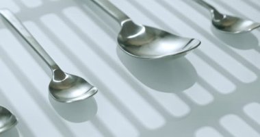 extreme close-up, detailed. large and small stainless steel spoons on a white glossy surface