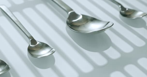 Extreme close-up, detailed. large and small stainless steel spoons on a white glossy surface — Stockvideo